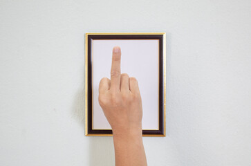 The right hand holds up the middle finger, placed inside an empty wooden picture frame.