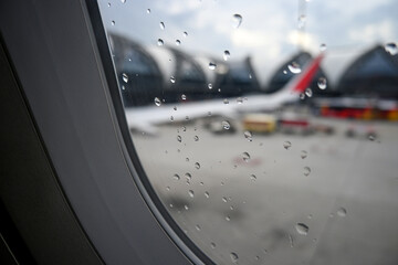 Rain Drops on Airplane Window with Airport Background and Aircraft in Hazy Weather Conditions