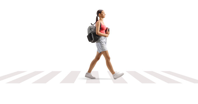 Full length profile shot of a female teenage student walking at a zebra crossing