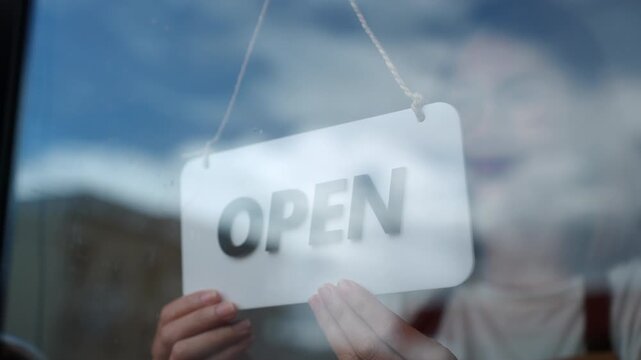 Close-up Happy Owner or waitress in apron turns the sign from closed to open, welcoming customers to a new cafe and small business restaurant in the morning. New business coffee shop cafe.
