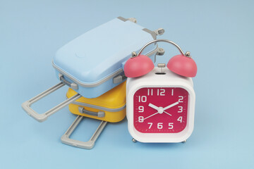 Red and white alarm clock with two suitcases on blue background.