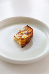Single toasted croissant slice with melted butter served on minimalist white ceramic plate with soft daylight on clean background