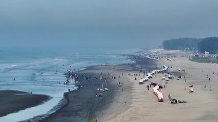 Cox's Bazar, Bangladesh - 20 August 2025: Aerial view of the extensive sandy beach crowded with people and dotted with colorful umbrellas and stalls.