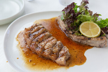 Sliced pork steak in brown pepper sauce garnished with lemon and fresh leafy greens on a white plate, bright and minimal dining setting