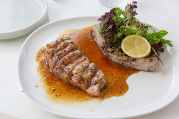 Grilled pork steak plated with brown sauce and a lemon slice, paired with fresh salad greens on a white plate under natural light