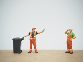 Naklejka premium Mini toy of action figure with blurred background. Miniature diorama photography concept design. Minifigure of cleaning crew character wearing orange suit with truck and garbage bin.