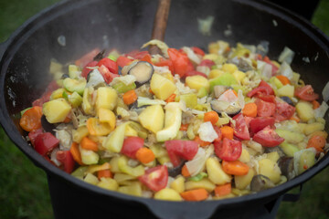 The food is cooked in a large frying pan. Stewing vegetables for rice. Cooking a lot of food outside.