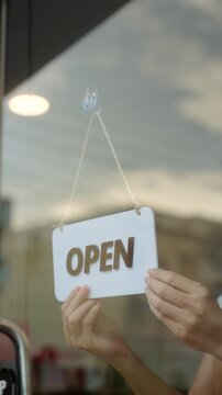 Close-up Happy Owner or waitress in apron turns the sign from closed to open, welcoming customers a new cafe and small business restaurant in morning. New business coffee shop cafe. Vertical video.