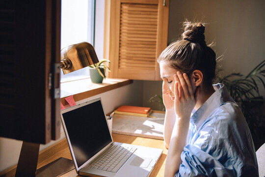 Tired young woman has closed her eyes and is sitting in front of a computer. The freelancer took a break from work due to a headache.
