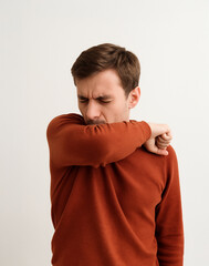 Young man coughing or sneezing into his elbow, showing correct etiquette to prevent the spread of infection. Health care, cold and flu prevention concept on white background