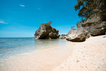 View of the serene beach revealing a tranquil scene where turquoise waters meet the white sand, as weathered rocks stand as silent sentinels, Guimaras, Western Visayas, Philippines.