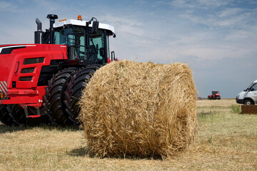 Obraz premium A roll of dry hay lies in a field after harvesting against the background of a modern tractor.