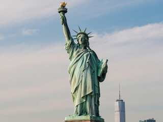 Obraz premium Full close-up view of the Statue of Liberty on Liberty Island, New York City. The monument stands tall against the sky with the One World Trade Center rising in the distance, symbolizing freedom