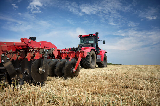Rear view of a large tractor with a disk harrow plow standing in a field. Start tillage after harvest.
