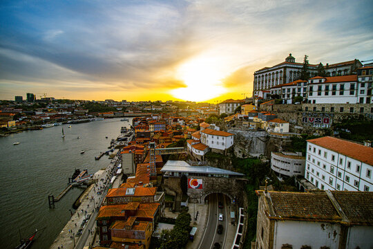 Aerial view of terracotta rooftops cascade towards the Douro River under a golden sunset, framing the Dom Lu&Atilde;&shy;s I Bridge and Ribeira district, Porto, Portugal.