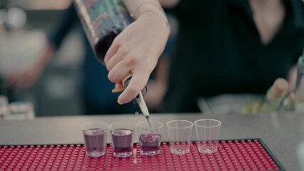 Close-up of bartender hand pouring vodka from bottle into shot glasses on the counter in a nightclub or bar. Concept of party, alcohol, nightlife, celebration, drinks service.