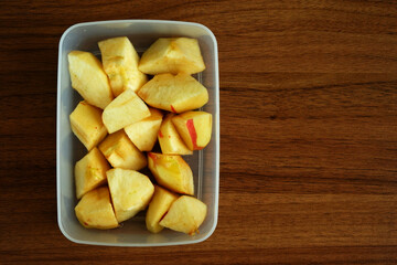 A delicious top-down view of sliced apples in a transparent white lunchbox, ready to eat. The box is placed on a wooden table, perfect for healthy food, snack, and nutrition themes.