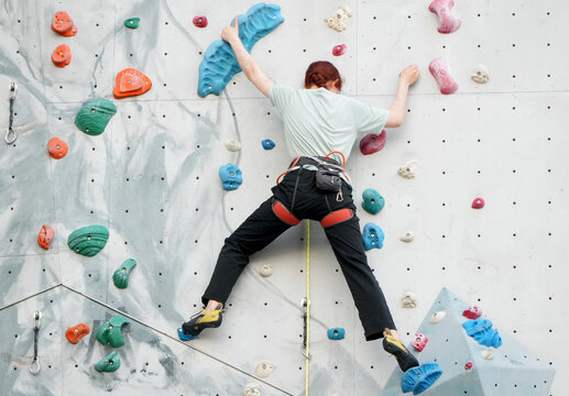 a woman is rock climbing on a colorful artificial wall.