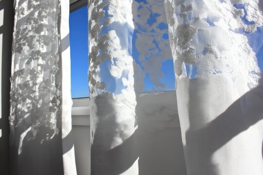 Sheer white lace curtains billow gently in a sunny room, revealing a clear blue sky - Powered by Adobe