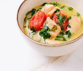 A warm bowl of creamy seafood soup features tender pieces of salmon, vibrant cherry tomatoes, and fresh herbs. This comforting dish is perfect for a cozy meal at home.