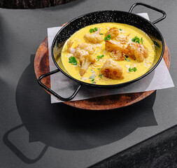 Delicious dish served in a black pan on a wooden plate