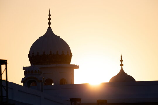 View of the Gurdwara bathed in the golden hues of the setting sun, its domes silhouetted against the sky in Kartarpur, Punjab, Pakistan.