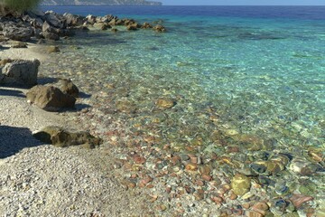 Clear turquoise water laps a pebbly beach, rocks in foreground
