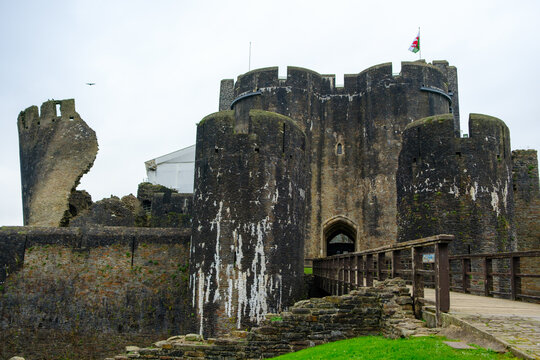 View of the imposing Caerphilly Castle, with its weathered stone walls, towering gatehouse, and the Welsh flag fluttering above, Caerphilly, Wales, United Kingdom.