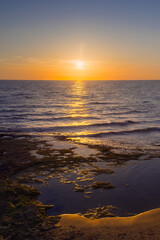 Vibrant Sunset Reflecting on Shimmering Ocean Waves by the Rocky Shore