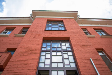 Fototapeta premium Bright red brick building stands tall against a blue sky with scattered clouds in an urban setting