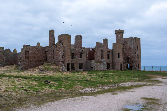 View of the crumbling stone walls of New Slains Castle stand against the grey skies and the distant blue sea, a stark reminder of history, Peterhead, Scotland, United Kingdom.