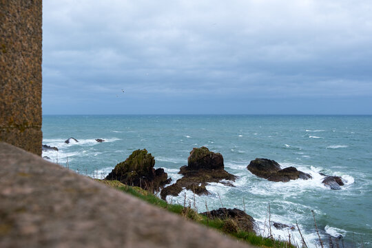 View of rugged rocks meet the turbulent sea under a moody sky, the scene framed by the weathered stone of the castle, Peterhead, Scotland, United Kingdom.