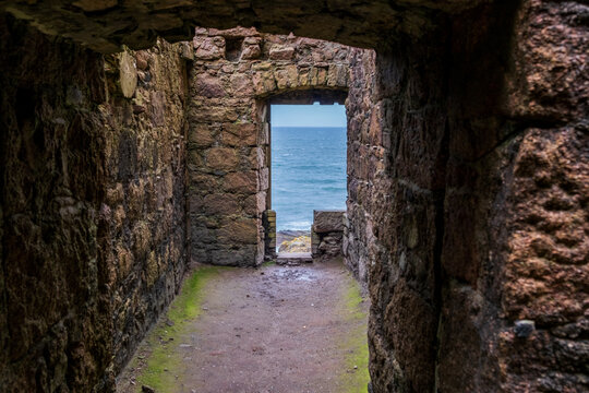 View of an aged stone passage reveals the vast ocean beyond, moss clinging to the walls, a testament to time's passage, Peterhead, Scotland, United Kingdom.