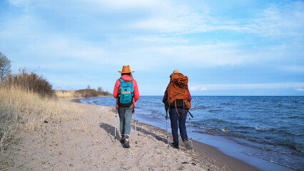Two people are walking along the beach along the lake, view from the back. Two girlfriends are looking for a camping spot. Travel and adventures