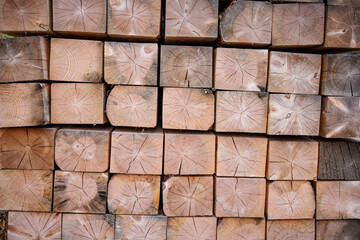 A folded bar in a stack. The end part is made of treated wooden beams. Background with a wood texture. Industrial texture of lumber. A close-up background image of a stack of wooden beams.