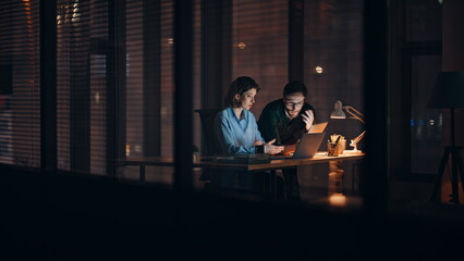 Overloaded partners brainstorming night office looking laptop. Two colleagues