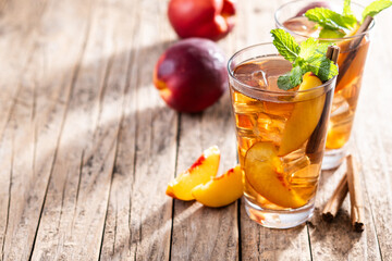 Refreshing peach iced tea in glass with ice cubes and cinnamon on wooden table. Copy space
