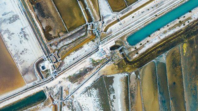 Aerial view of geometric salt pans reflecting varied hues under the sun, creating an abstract mosaic of earth tones and turquoise waters, Pag, Zadar County, Croatia.