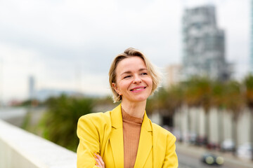 Smiling woman in a yellow blazer standing outdoors in the city with arms crossed