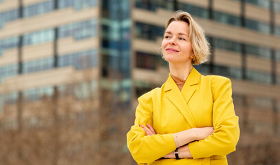 Confident woman in yellow blazer standing with arms crossed in the city.