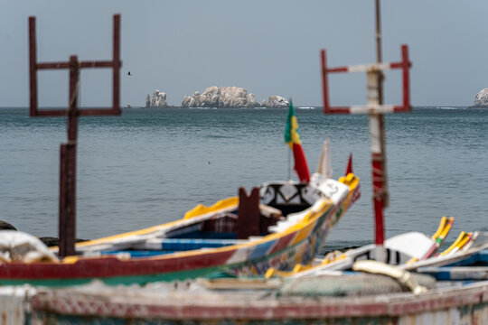 Dakar, Senegal - 12 May 2025: View of vibrant fishing boats resting on the sandy shore, their colorful hulls contrasting with the distant, hazy islands and calm, gray sea.