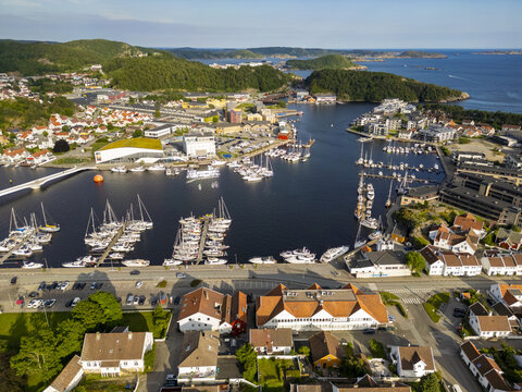 Aerial view of boats dotting the deep blue harbor contrasting with the terracotta roofs and lush green hillsides, Mandal, Agder, Norway.