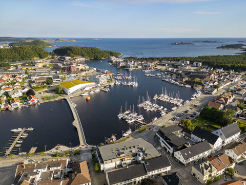 Aerial view of boats nestled in the dark harbor waters, reflecting the sky, while buildings cluster along the shore, Mandal, Agder, Norway.