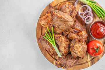 Grilled pork pieces served with onion rings and tomato sauce on wooden plate. top view. copy space