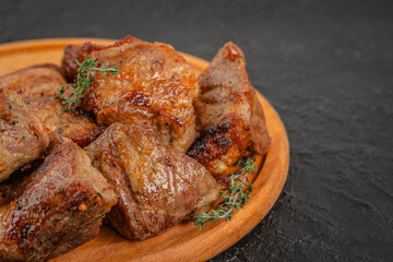Close-up of grilled pork shashlik pieces on wooden plate with herbs