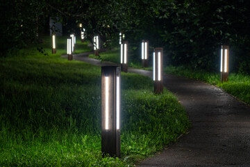 Tranquil nighttime park path illuminated by series of modern, rectangular bollard lights, casting...
