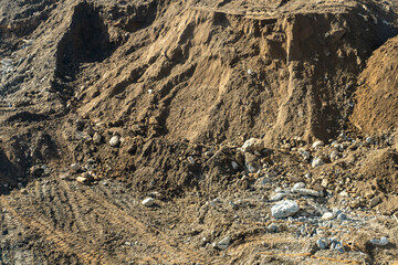 Rugged and textured landscape of construction site with mounds of earth, sand, rocks, and visible tire tracks under natural sunlight