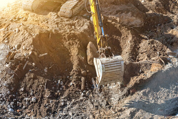 Powerful yellow hydraulic excavator diligently digging into massive pile of brown earth, rocks, and mixed construction debris under bright, sunny conditions at active demolition or building preparatio