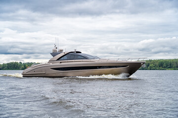 Sleek golden motor yacht gracefully cruising on tranquil waters under cloudy sky, showcasing modern luxury design and creating dynamic wake