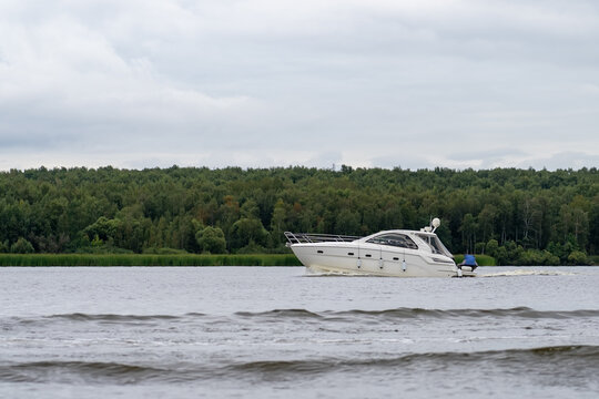 White motor yacht cruising on tranquil water with lush green forest on distant shore under overcast sky - Powered by Adobe